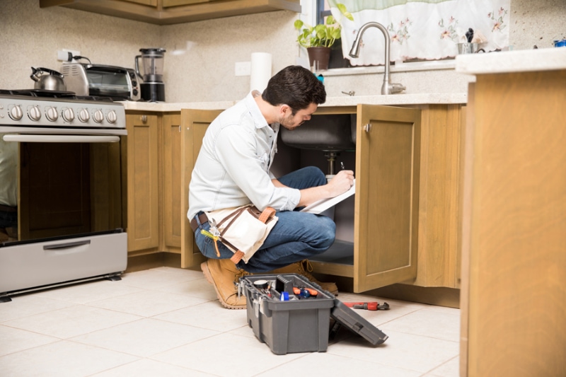 What Should I Do About Frozen Pipes? Image is a photograph of a plumbing professional looking under the sink.