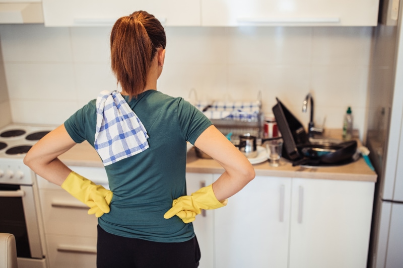 How Often Do I Need to Clean My Main Sewer Line? Young woman is standing in the kitchen, wearing protective gloves, ready from washing dishes.